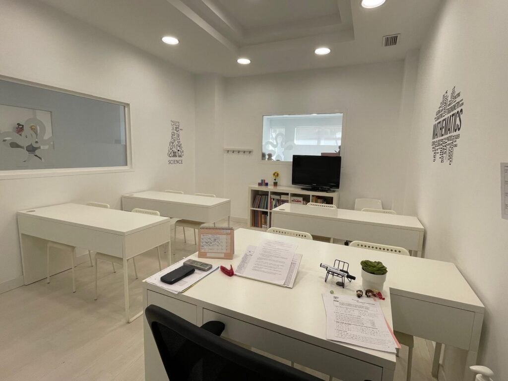 Aula con mesas blancas, pizarra y mobiliario educativo