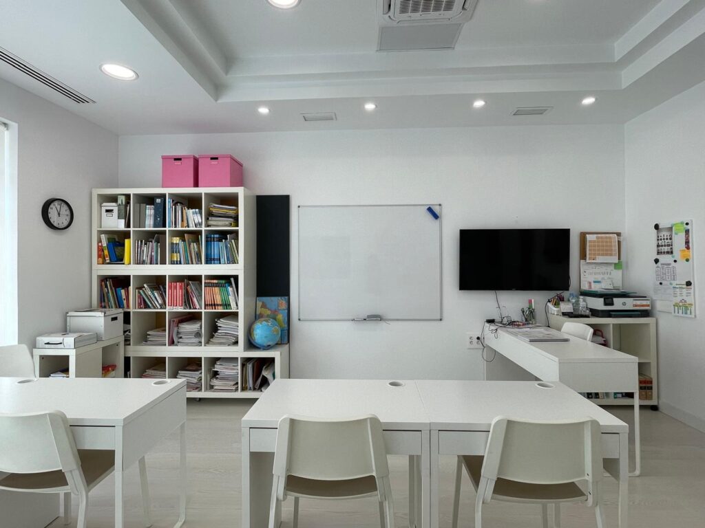 Aula de eduCa con mesas de estudio y estantería con libros y materiales